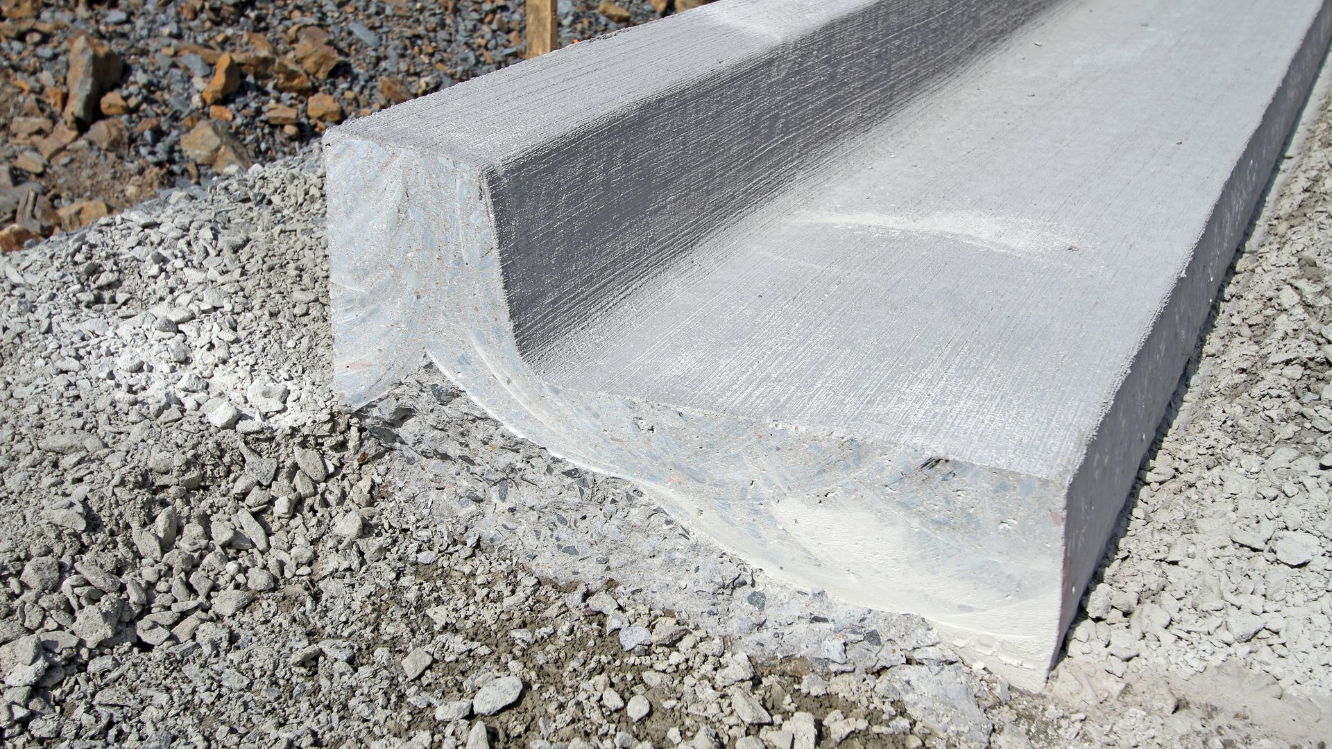Concrete road curb with textured surface resting on gravel construction site