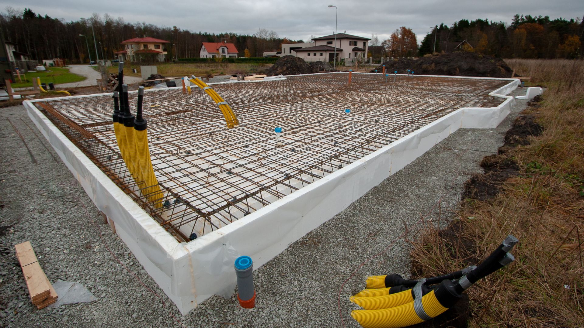 Concrete foundation with rebar grid and yellow utility pipes on construction site