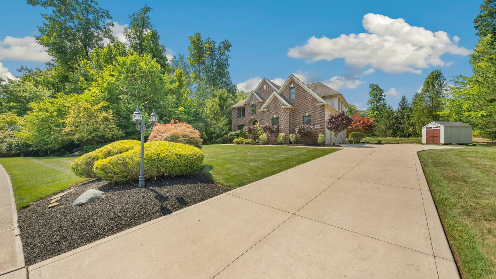 Brick house with manicured lawn, landscaped yard, and small shed on sunny day
