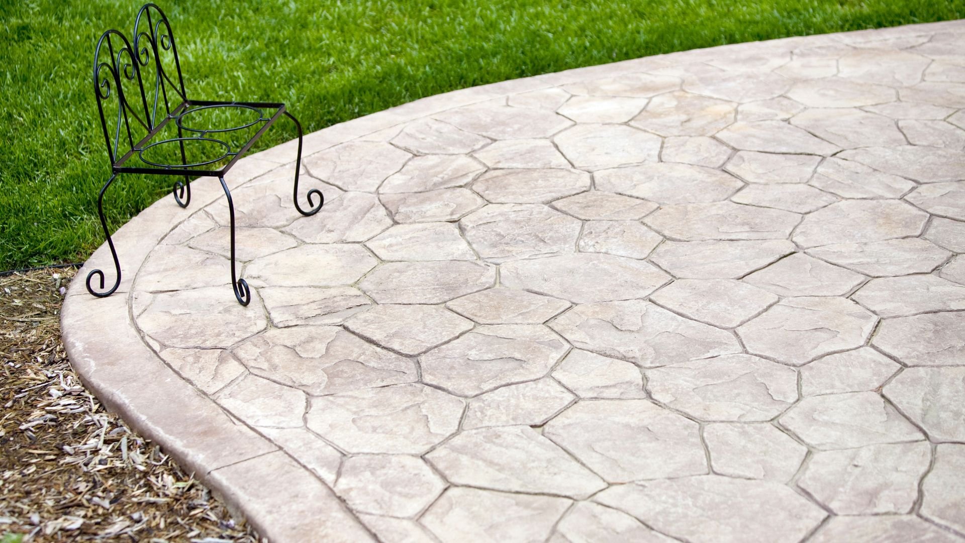 Wrought iron chair on textured stone patio with green grass background